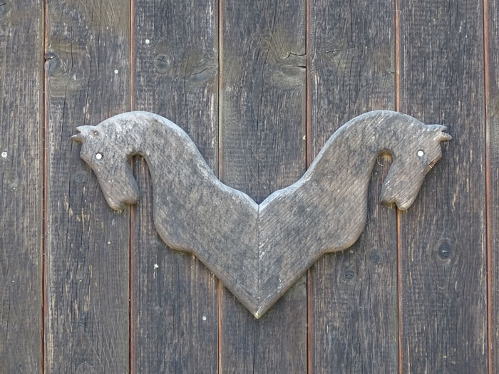 Zwei gespiegelte geschnitzte Holzpferdeköpfe auf Holztür