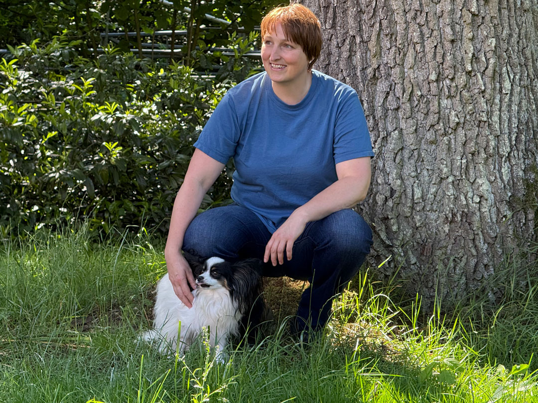 Ines Sander in der Hocke auf Wiese mit kleinem Hund